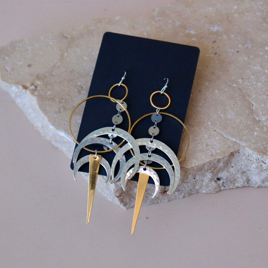 Pair of earrings with gold and silver crescent moon designs on a gray background